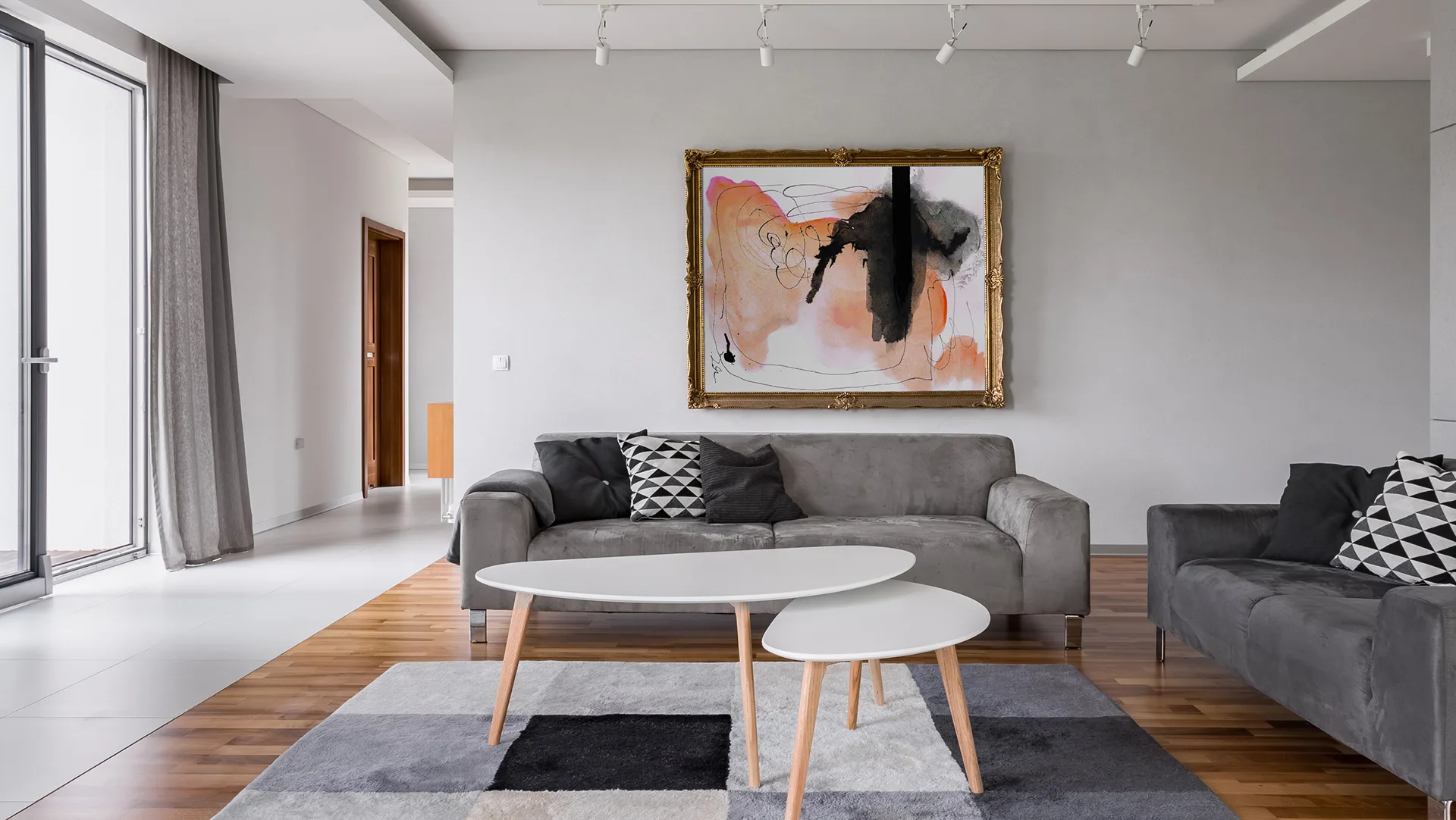 A contemporary living room with grey sofa, abstract framed art, and a polished hardwood floor