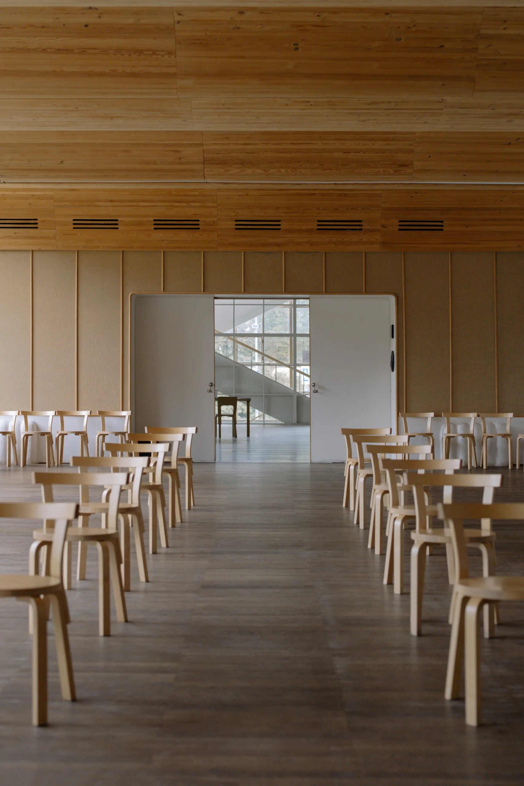 Bright community hall interior with light wood floor, simple chairs and natural light through tall windows
