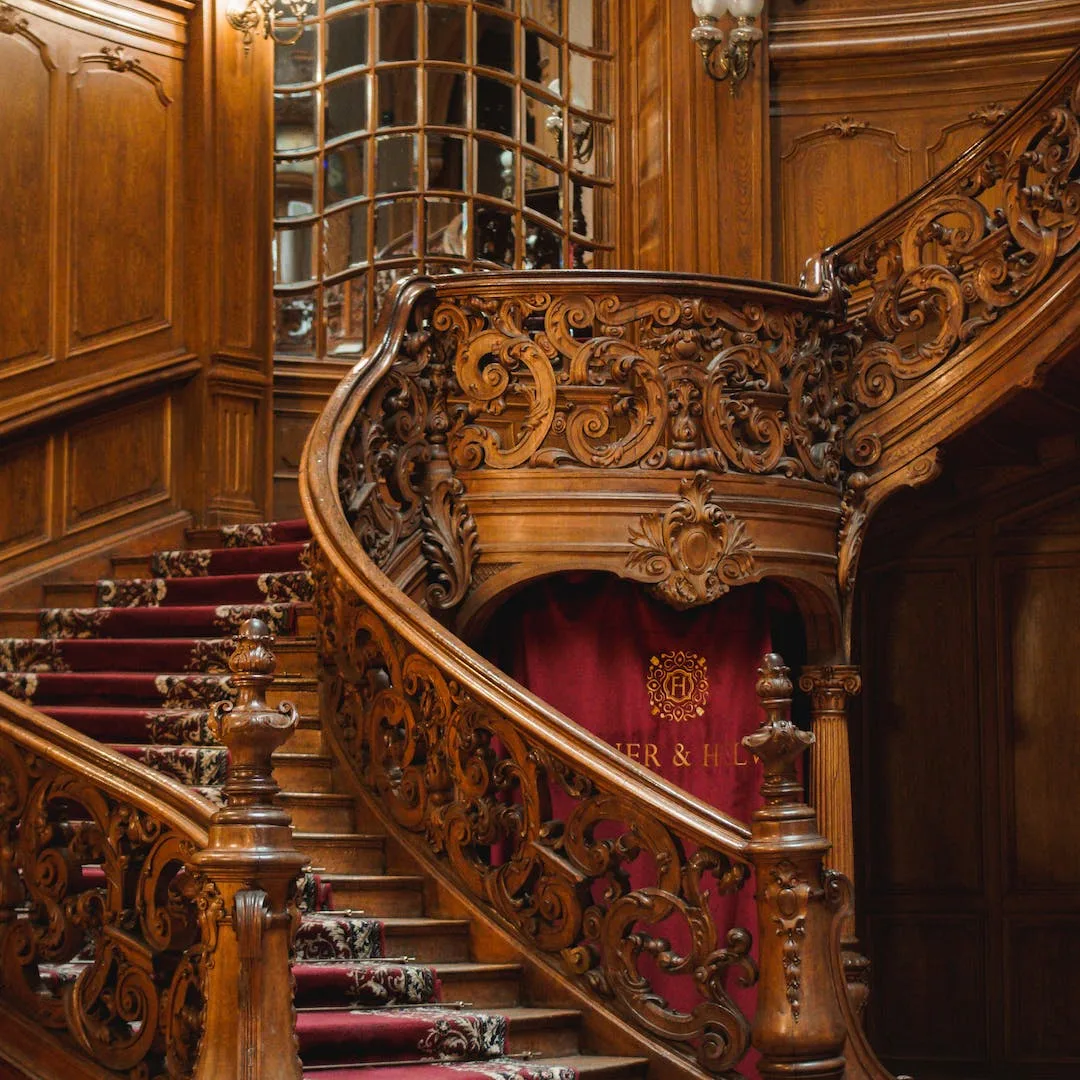 Ornate carved wooden staircase with red carpet in a heritage building