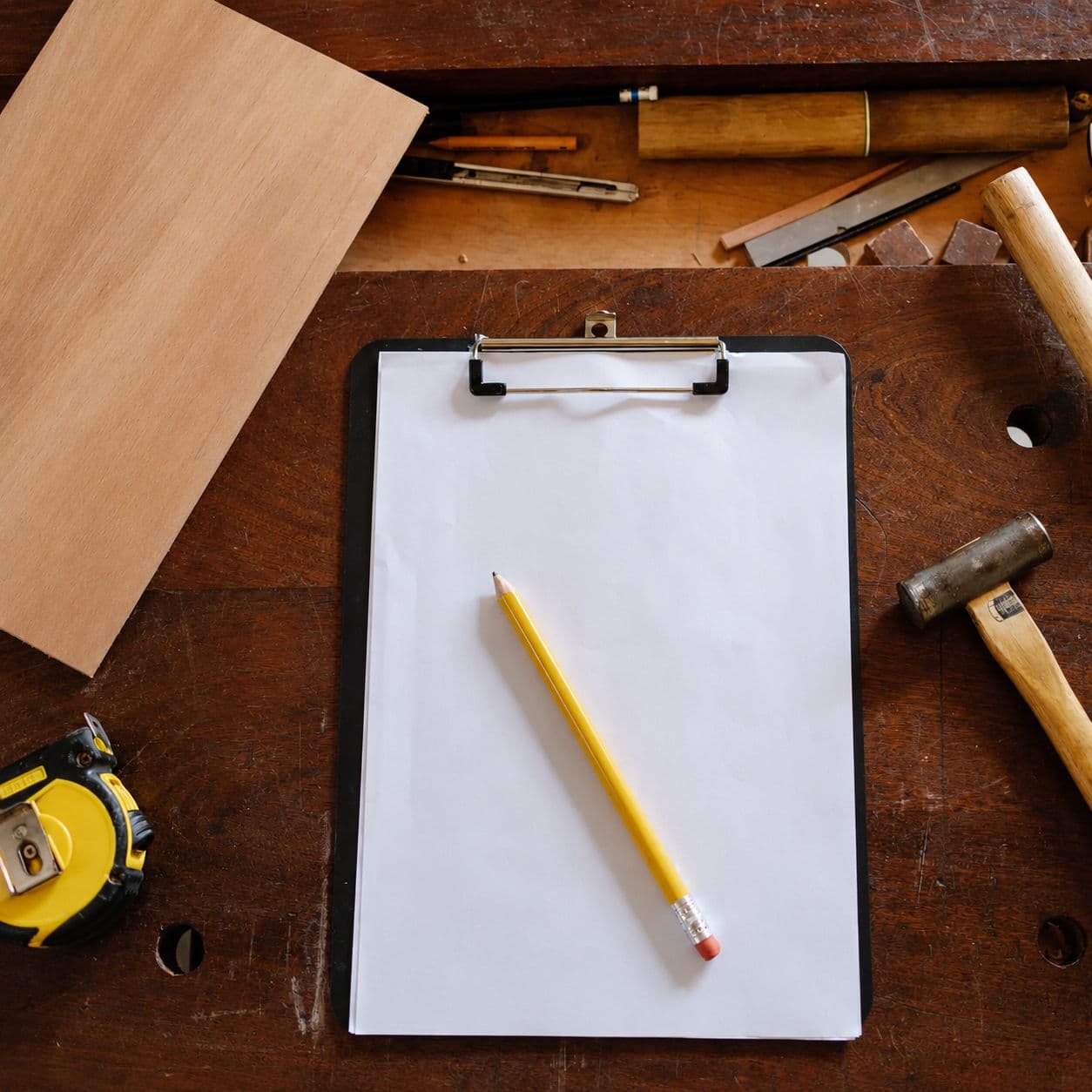 Clipboard, pencil and hand tools laid out on a workbench during a floor consultation