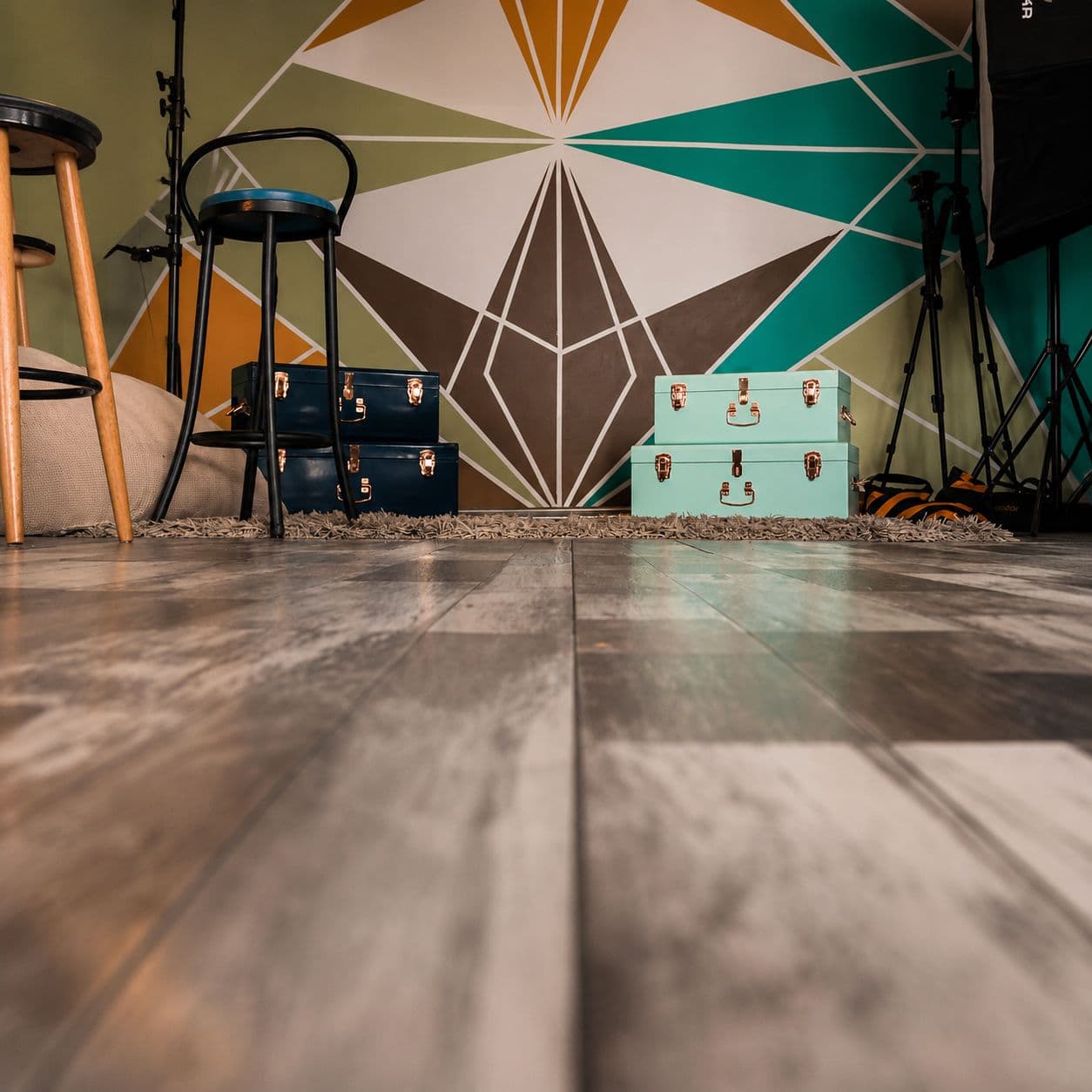Restored wood floor in a colourful interior with geometric wall mural and vintage trunks