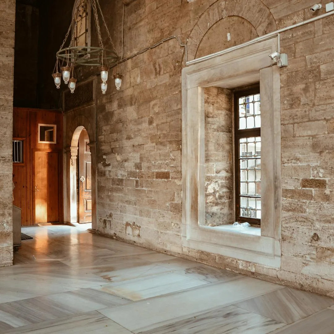 Stone-walled heritage interior with tall arched windows, pendant lights and a restored wood floor